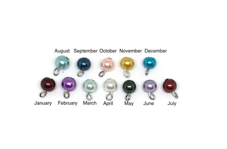 May include: A collection of twelve pearl beads in various colors, each with a silver loop. The months of the year are labeled above and below the beads, from January to December. The beads are in shades of blue, pink, purple, green, and gold.