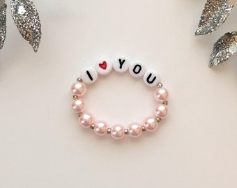 May include: A pink beaded bracelet with white letter beads spelling "I love you" with a red heart bead.
