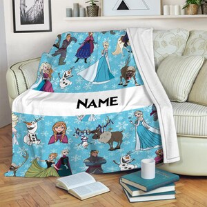 Pu&ograve; includere: Una coperta in pile azzurra con un motivo ripetuto di personaggi del film Frozen, tra cui Elsa, Anna, Olaf, Kristoff e Sven, su uno sfondo bianco con fiocchi di neve e una fascia orizzontale bianca centrale che riporta la parola NAME.
