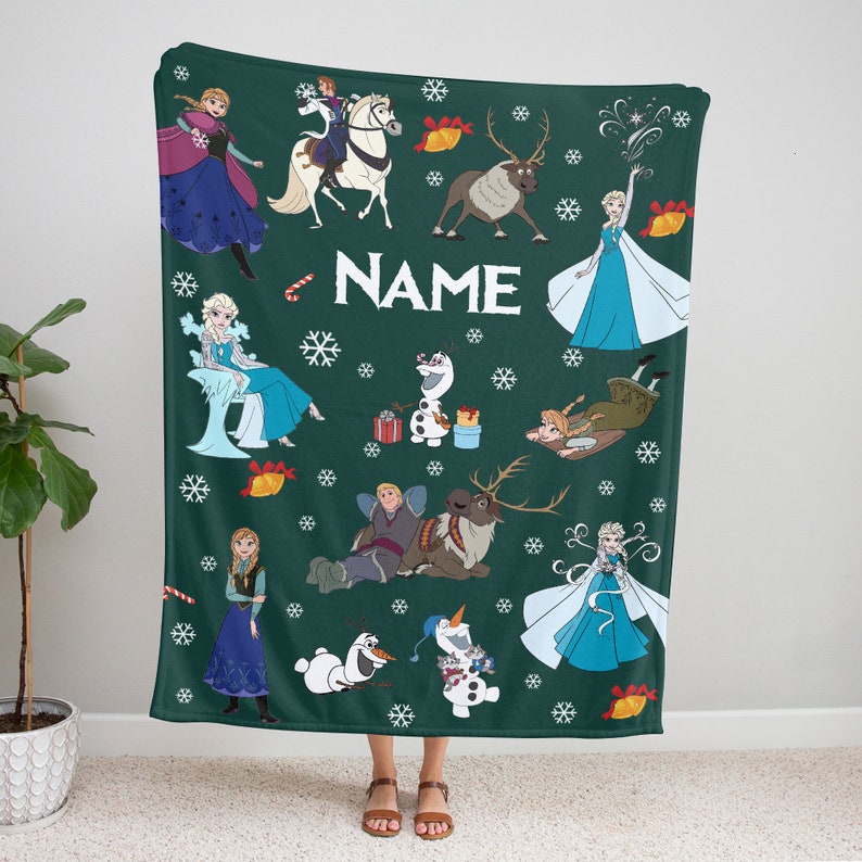 May include: A dark green fleece blanket featuring a repeating pattern of characters from the movie Frozen, including Elsa, Anna, Olaf, Kristoff, and Sven. The design includes white snowflakes, red and gold bells, candy canes, and the word NAME.