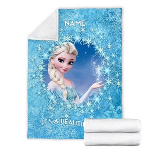 Pu&ograve; includere: Una coperta in pile blu con la grafica di un personaggio biondo con una treccia, circondato da una cornice circolare di fiocchi di neve bianchi e blu. Il testo NAME &egrave; stampato in alto e il testo IT'S A BEAUTI &egrave; stampato in basso.