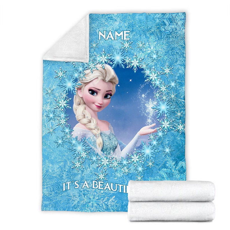 Pu&ograve; includere: Una coperta in pile blu con la grafica di un personaggio biondo con una treccia, circondato da una cornice circolare di fiocchi di neve bianchi e blu. Il testo NAME &egrave; stampato in alto e il testo IT'S A BEAUTI &egrave; stampato in basso.