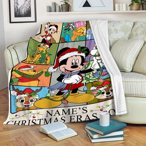 May include: A colorful Christmas-themed throw blanket featuring Mickey Mouse and friends. The blanket has a grid design with various cartoon characters in festive attire, with the text "NAME'S CHRISTMAS ERAS" at the bottom.