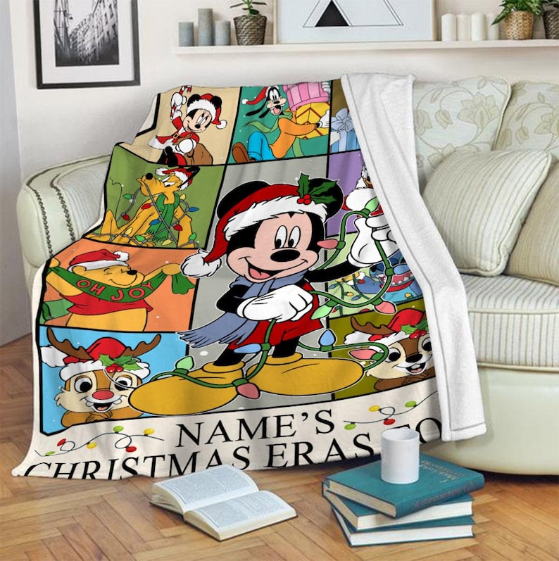 May include: A colorful Christmas-themed throw blanket featuring Mickey Mouse and friends. The blanket has a grid design with various cartoon characters in festive attire, with the text "NAME'S CHRISTMAS ERAS" at the bottom.