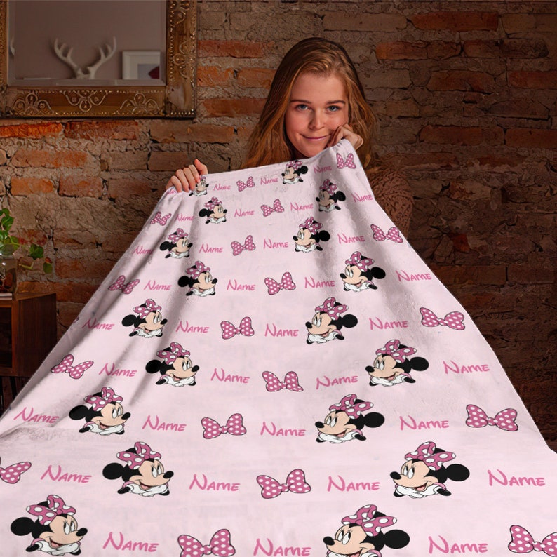 May include: A pink fleece blanket with a repeating pattern of a cartoon character with a pink bow and white polka dots. The character's name is repeated throughout the blanket.