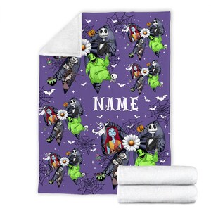 Puede incluir: Una manta morada con personajes de Pesadilla antes de Navidad. El dise&ntilde;o incluye a Jack Skellington, Sally, Oogie Boogie y otros elementos. La palabra "NAME" est&aacute; impresa en la manta. Dos mantas blancas dobladas est&aacute;n en la parte inferior.