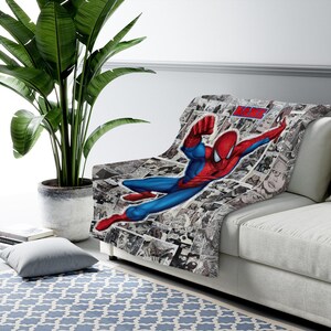 May include: A soft throw blanket featuring a vibrant, full-color illustration of Spider-Man in a dynamic flying pose, set against a black and white comic book panel background. The blanket includes a red and blue text box with the word NAME.