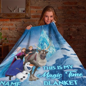 May include: A blue fleece blanket featuring characters from Frozen, including Elsa, Anna, Kristoff, Sven, and Olaf, set against an icy castle background. The text reads, "THIS IS MY Magic Time BLANKET" with a placeholder for a name at the bottom.
