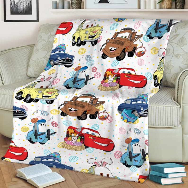 May include: A white fleece throw blanket with a repeating pattern of cartoon cars from the Cars movie franchise. The cars are decorated with Easter eggs and bunnies. The blanket features characters like Lightning McQueen, Mater, and Tow Mater.
