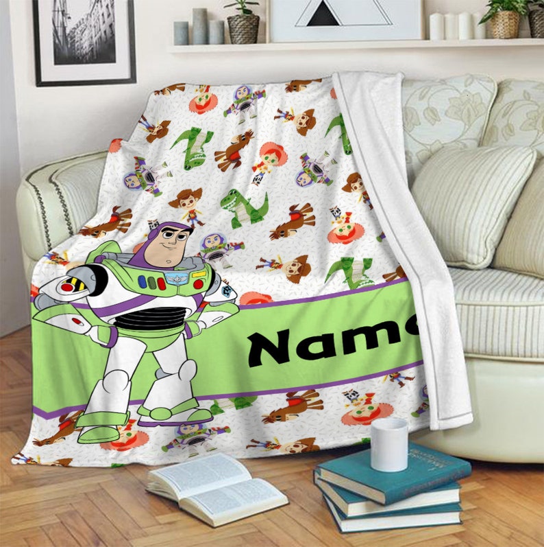 May include: A white fleece blanket featuring a repeating pattern of Toy Story characters including Buzz Lightyear, Woody, Jessie, and Rex. A large Buzz Lightyear figure stands on the left, next to a wide lime green horizontal band with the text Name.