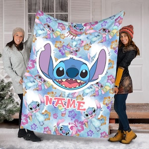 Puede incluir: Una manta de forro polar azul claro con un patr&oacute;n repetitivo del personaje Stitch comiendo helado y usando gafas de sol, con un gr&aacute;fico central grande de la cara de Stitch y la palabra NAME impresa en letras rosas entre flores de hibisco.