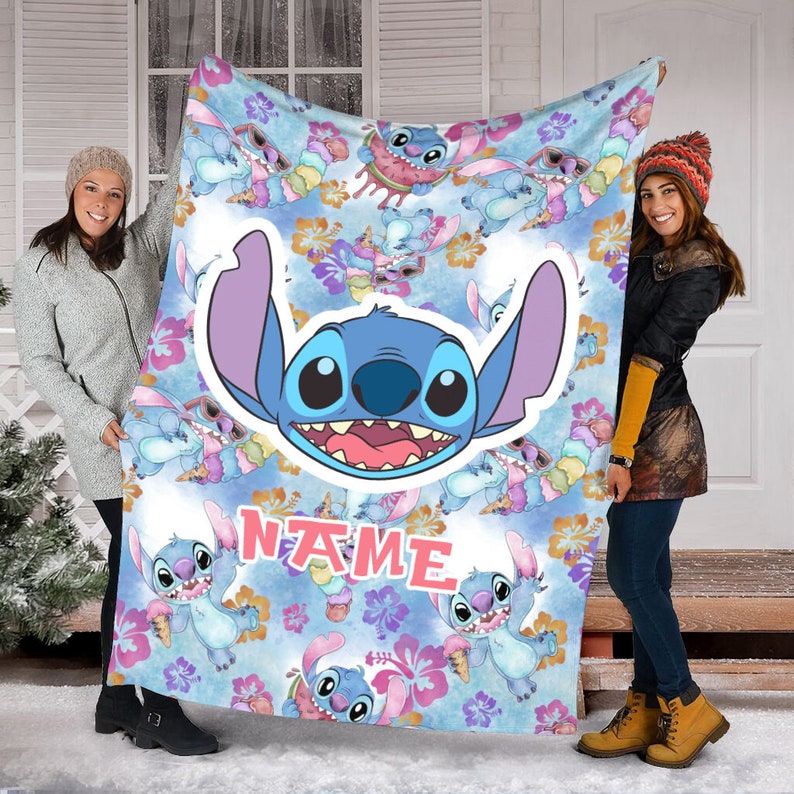 Puede incluir: Una manta de forro polar azul claro con un patr&oacute;n repetitivo del personaje Stitch comiendo helado y usando gafas de sol, con un gr&aacute;fico central grande de la cara de Stitch y la palabra NAME impresa en letras rosas entre flores de hibisco.