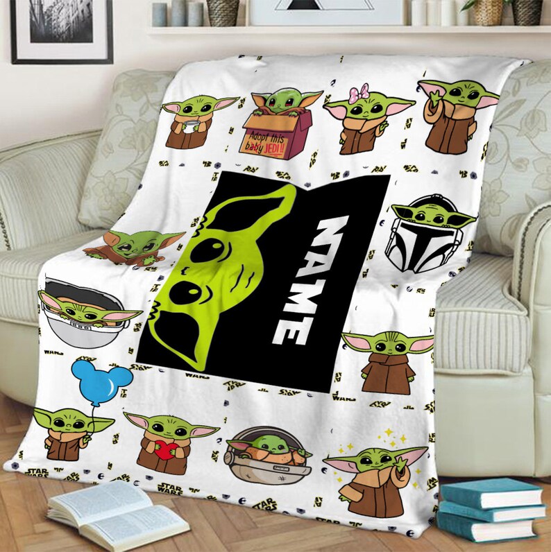 May include: A white throw blanket featuring a repeating pattern of green alien characters in brown robes. The design includes a large black rectangular center panel with the word NAME in white text and a box labeled Adopt this baby JEDI.
