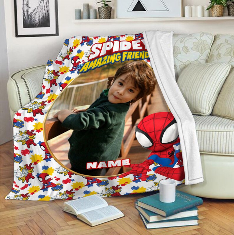 K&ouml;nnte beinhalten: Eine wei&szlig;e Fleecedecke mit einem sich wiederholenden Muster aus Spidey and His Amazing Friends-Figuren, roten und gelben Sternen sowie blauen Spinnennetz-Grafiken. Ein gro&szlig;er kreisf&ouml;rmiger Rahmen in der Mitte zeigt ein Kinderfoto mit dem Text NAME.