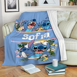 May include: A light blue fleece throw blanket featuring the character Stitch from Lilo & Stitch, surrounded by tropical flowers and green leaves. The name Sofia is printed in large white letters across a horizontal band in the center of the blanket.