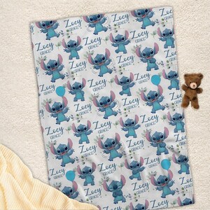 May include: A white fleece blanket featuring a repeating pattern of the blue character Stitch, small green leaves, and the name Zoey Grace in a cursive blue font. A small brown teddy bear is positioned to the right of the rectangular blanket.