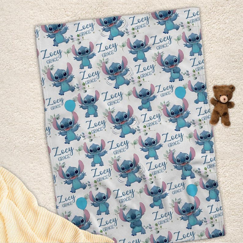 May include: A white fleece blanket featuring a repeating pattern of the blue character Stitch, small green leaves, and the name Zoey Grace in a cursive blue font. A small brown teddy bear is positioned to the right of the rectangular blanket.