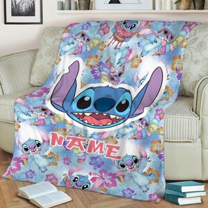 Puede incluir: Una manta suave con un patr&oacute;n repetitivo del personaje azul Stitch, flores de hibisco rosas y conos de helado sobre un fondo azul claro. Se incluye un gr&aacute;fico central grande del rostro de Stitch y la palabra NAME impresa.