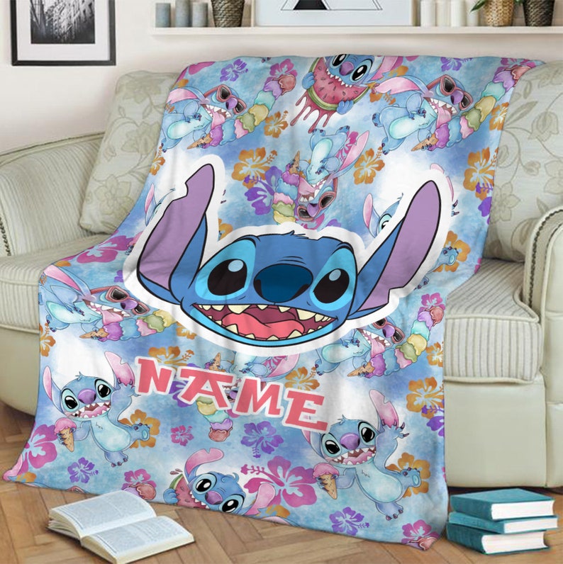 Puede incluir: Una manta suave con un patr&oacute;n repetitivo del personaje azul Stitch, flores de hibisco rosas y conos de helado sobre un fondo azul claro. Se incluye un gr&aacute;fico central grande del rostro de Stitch y la palabra NAME impresa.