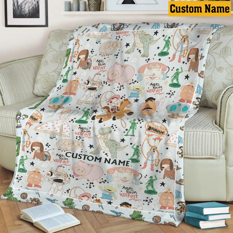 K&ouml;nnte beinhalten: Eine wei&szlig;e Fleecedecke mit einem wiederkehrenden Muster aus Zeichentrickfiguren, darunter ein Weltraum-Ranger, ein Cowboy, ein Cowgirl, ein Dinosaurier, ein Schwein und gr&uuml;ne Plastiksoldaten. Der Text "ANDY'S ROOM KEEP OUT" ist darauf zu sehen.
