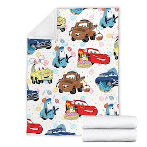 May include: A white fleece blanket with a colorful pattern of cartoon cars and Easter eggs. The cars are from the Disney Pixar movie Cars. The cars are red, blue, yellow, and brown. The eggs are pink, blue, green, and yellow.