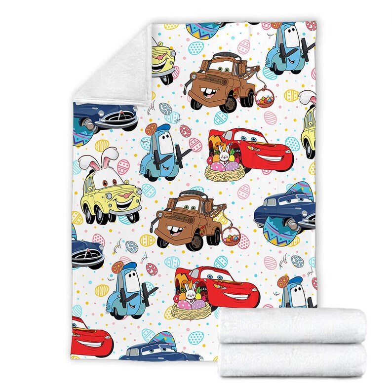 May include: A white fleece blanket with a colorful pattern of cartoon cars and Easter eggs. The cars are from the Disney Pixar movie Cars. The cars are red, blue, yellow, and brown. The eggs are pink, blue, green, and yellow.