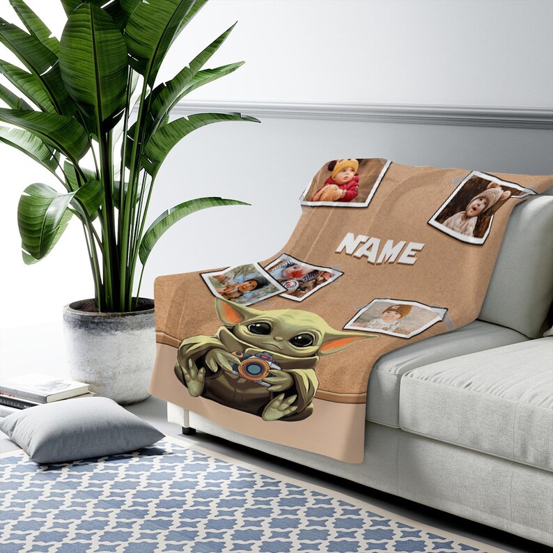 May include: A brown fleece blanket with a cartoon image of a green baby Yoda holding a camera. The blanket has a corkboard background with several photos of children attached to it. The text "NAME" is printed on the blanket.