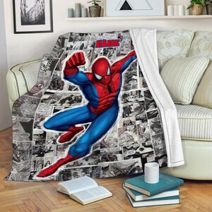 May include: A soft throw blanket featuring a large, colorful illustration of Spider-Man in a dynamic pose over a black and white comic book panel background. The blanket includes a red text box at the top with the word NAME in bold blue letters.