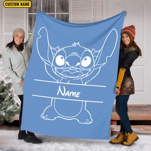 May include: A light blue fleece blanket featuring a large white line art illustration of the character Stitch with arms raised. A horizontal white banner across the center contains the word Name in white script. A yellow box says CUSTOM NAME.