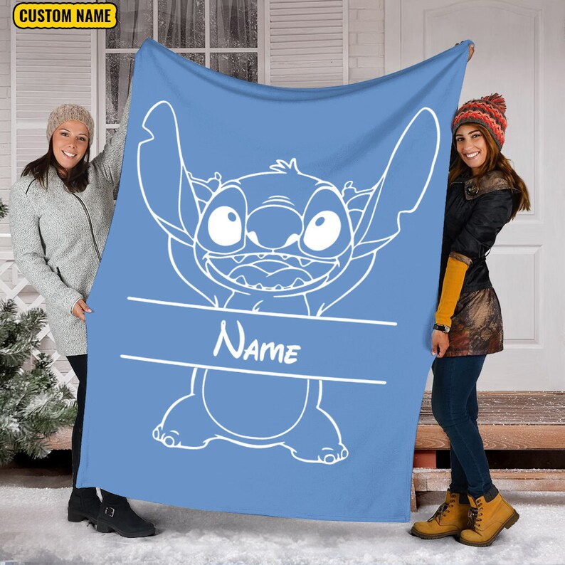 May include: A light blue fleece blanket featuring a large white line art illustration of the character Stitch with arms raised. A horizontal white banner across the center contains the word Name in white script. A yellow box says CUSTOM NAME.