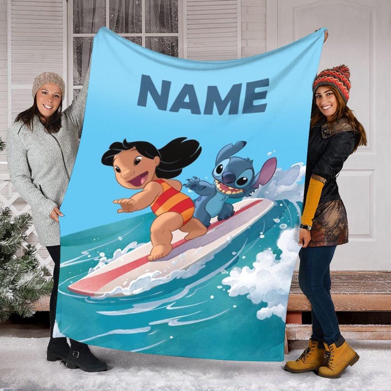 Peut inclure: Une couverture en polaire bleue et blanche avec un nom personnalis&eacute;, "NAME", et une image de dessin anim&eacute; de Stitch et Lilo faisant du surf sur une vague.