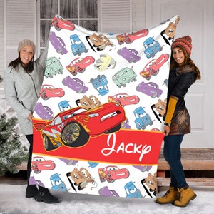 Pu&ograve; includere: Una coperta in pile bianca con un motivo ripetuto di varie auto da corsa a cartoni animati in rosso, blu, viola e marrone chiaro. Una grande auto da corsa rossa &egrave; mostrata sopra una fascia rossa con il testo corsivo bianco Jacky.
