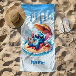 May include: A beach towel featuring a cartoon character relaxing on a tropical island with an umbrella. The towel has a blue and white design with the word "Name" printed on it. A straw hat and white flip-flops are next to the towel on a sandy surface.