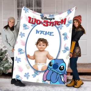 K&ouml;nnte beinhalten: Eine wei&szlig;e Fleecedecke mit dem Disney Lilo & Stitch Logo oben, einem zentralen ovalen Rahmen f&uuml;r ein Foto mit dem Text NAME dar&uuml;ber und einem wiederkehrenden Muster aus Stitch-Figuren, blauen Blumen und rosa Bl&auml;ttern auf dem Hintergrund.