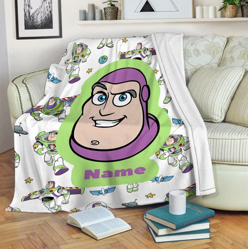 May include: A white fleece blanket featuring a repeating pattern of Buzz Lightyear in various poses, stars, and planets. A large central green graphic displays a cartoon portrait of Buzz Lightyear with the purple text Name printed below it.