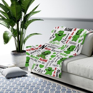 May include: White fleece blanket with a repeating pattern of green and red cartoon characters. The characters are a green monster with a stitched mouth and a red heart. The text "Name" is repeated throughout the pattern.