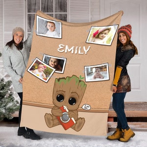 May include: A brown fleece blanket with a corkboard design featuring a cartoon character holding a camera. The blanket has a personalized name "EMILY" and several photos of babies.