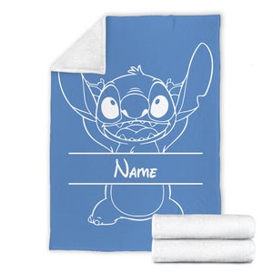 May include: A blue fleece blanket featuring a white line art illustration of the character Stitch with a wide grin. The design includes a horizontal banner area with the word Name printed in white text. The blanket has a white plush underside.