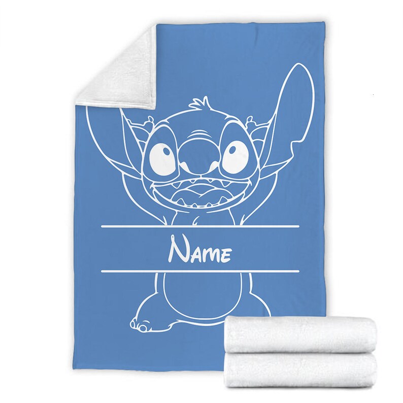 May include: A blue fleece blanket featuring a white line art illustration of the character Stitch with a wide grin. The design includes a horizontal banner area with the word Name printed in white text. The blanket has a white plush underside.
