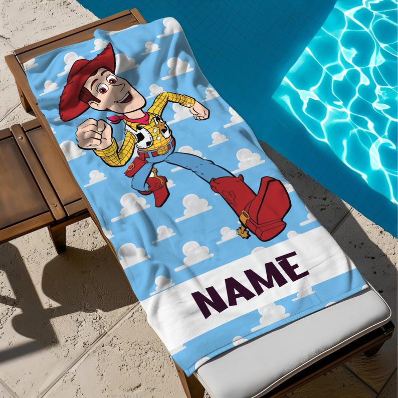 May include: A light blue beach towel with a cartoon cowboy character running across a sky-blue background with white clouds. The towel has a white stripe with the word "NAME" in black.