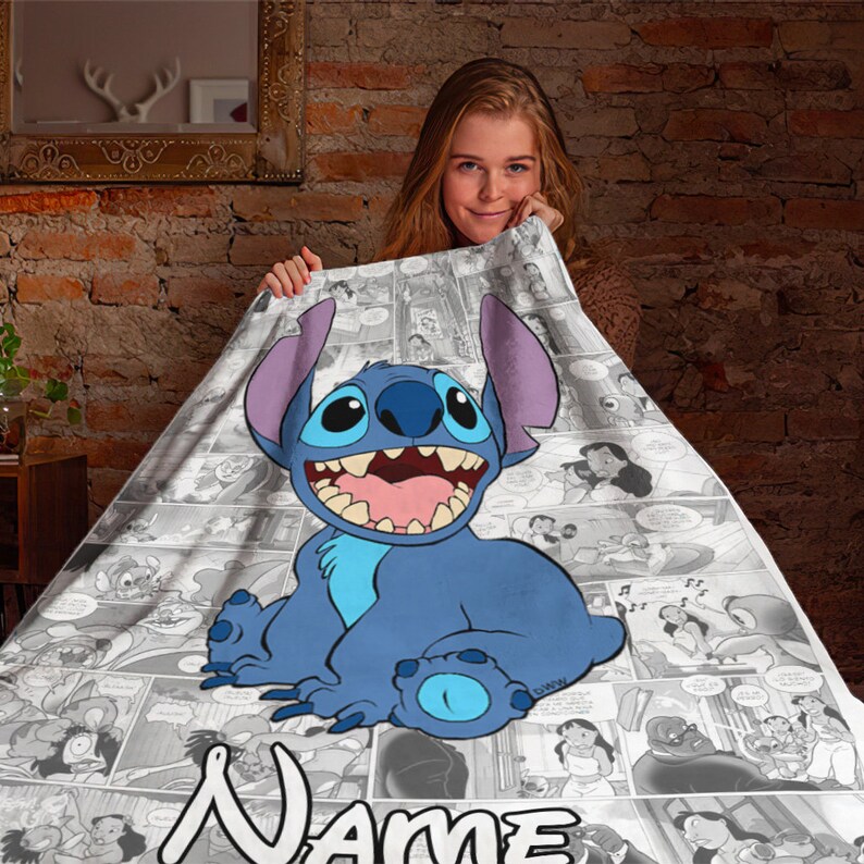 May include: A soft blanket featuring a large, colourful illustration of the blue character Stitch from Lilo and Stitch, centred over a black and white comic book panel background. The word Name is printed in large white letters at the bottom edge.