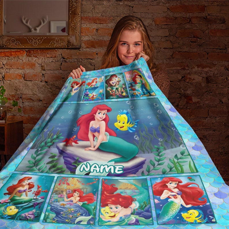 K&ouml;nnte beinhalten: Eine weiche Fleecedecke mit einer Collage von Arielle und Fabius aus Arielle, die Meerjungfrau. Das Design zeigt mehrere Unterwasserszenen, ein gro&szlig;es zentrales Bild von Arielle auf einem Felsen und den anpassbaren Text NAME.