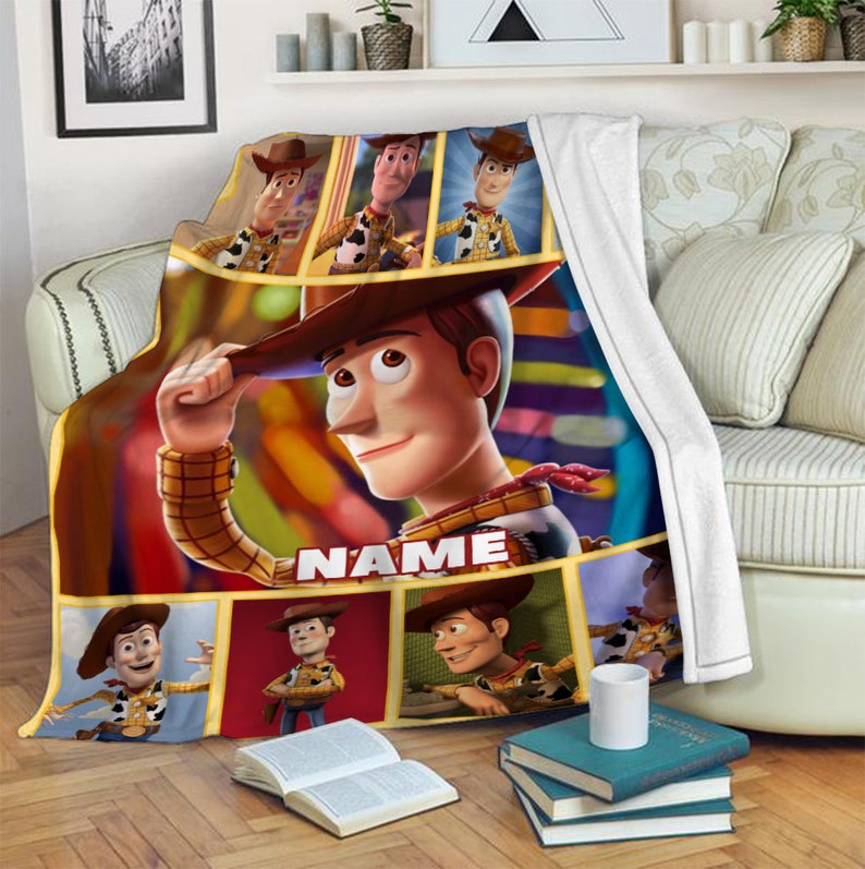 May include: A plush fleece throw blanket featuring multiple panels of the character Woody from Toy Story. The design includes a large central image of Woody tipping his hat, with the word NAME printed in white block letters below him.