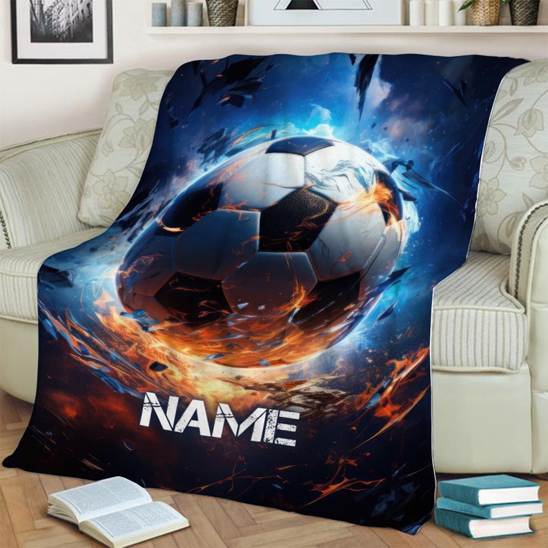 May include: A blue, orange, and white fleece blanket with a soccer ball in flames. The text "NAME" is printed on the blanket.