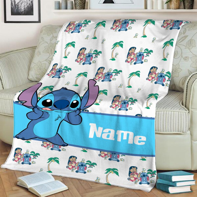 K&ouml;nnte beinhalten: Eine wei&szlig;e Fleecedecke mit einem sich wiederholenden Muster aus Lilo und Stitch-Figuren und Palmen. Ein breites blaues horizontales Band in der Mitte zeigt das Wort Name in wei&szlig;en Buchstaben, mit einer gro&szlig;en Stitch-Figur auf der linken Seite.