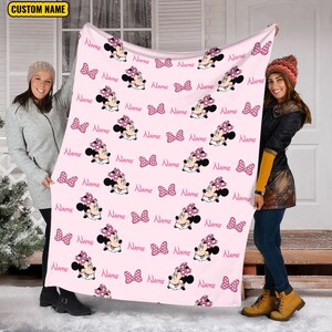 May include: Pink fleece blanket with a repeating pattern of Minnie Mouse wearing a pink polka dot bow. The blanket is personalized with the word "NAME" repeated throughout the pattern.