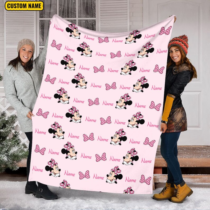 May include: Pink fleece blanket with a repeating pattern of Minnie Mouse wearing a pink polka dot bow. The blanket is personalized with the word "NAME" repeated throughout the pattern.