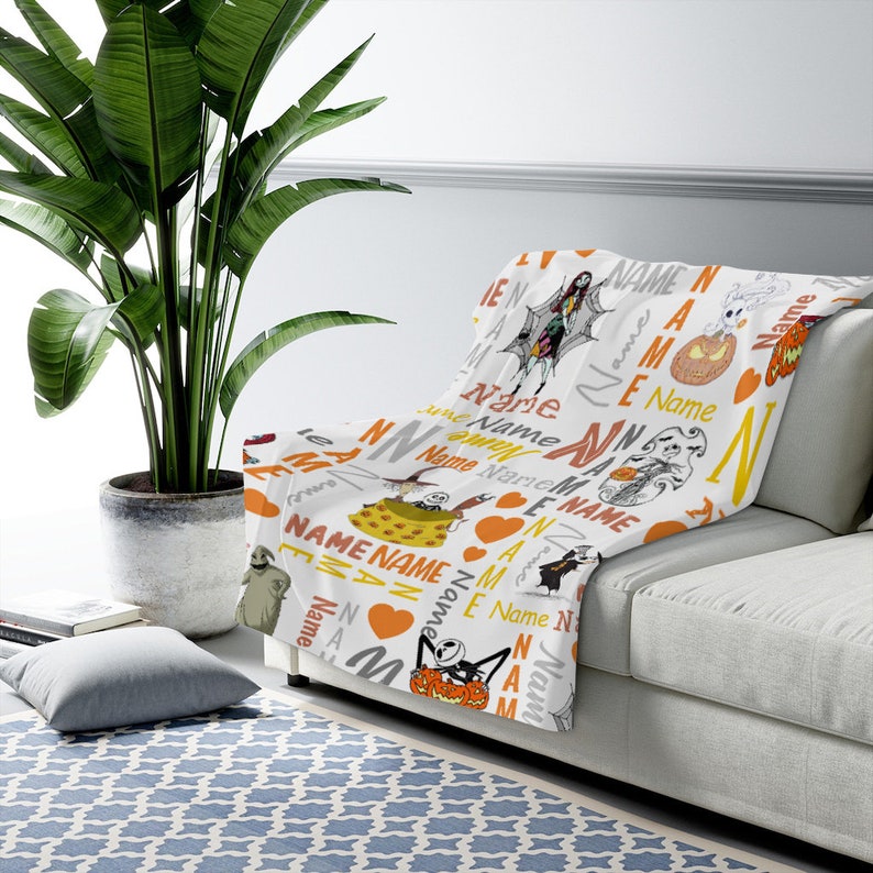 May include: A white throw blanket featuring a repeating pattern of characters from The Nightmare Before Christmas, including Jack Skellington, Sally, and Oogie Boogie, interspersed with orange hearts and the word Name in various fonts and colors.