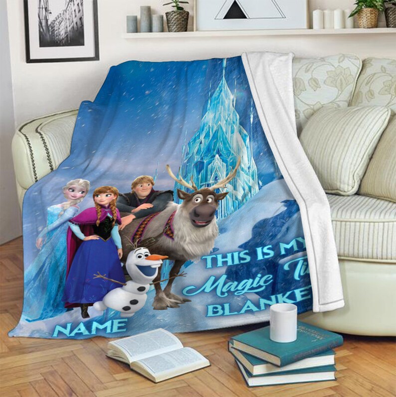 May include: A blue fleece throw blanket featuring a printed graphic of Elsa, Anna, Kristoff, Sven, and Olaf in front of an ice castle. The text reads THIS IS MY Magic TIME BLANKET and NAME. The blanket has a white underside and a soft texture.