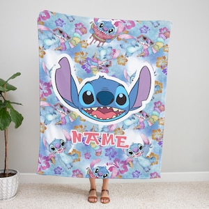 Puede incluir: Una manta de forro polar suave con un patr&oacute;n repetitivo del personaje azul Stitch comiendo helado y sand&iacute;a, intercalado con flores de hibisco rosas y naranjas sobre un fondo azul. Aparece una cara grande de Stitch y el texto NAME.
